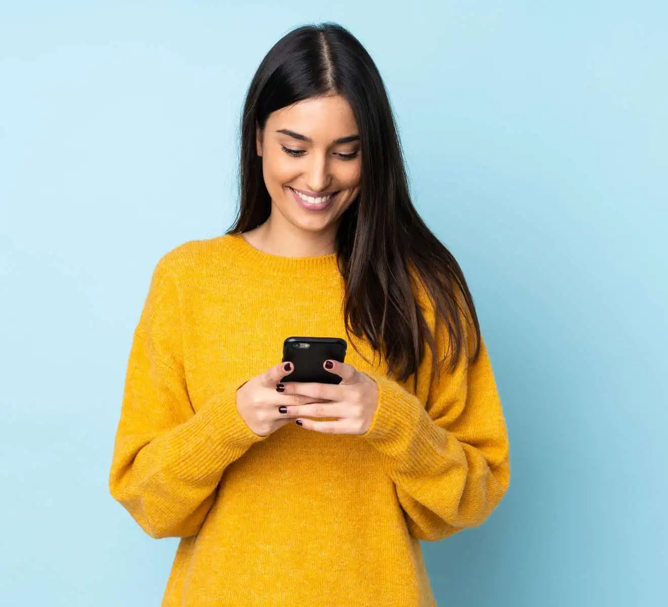 A woman is smiling while looking at a smartphone